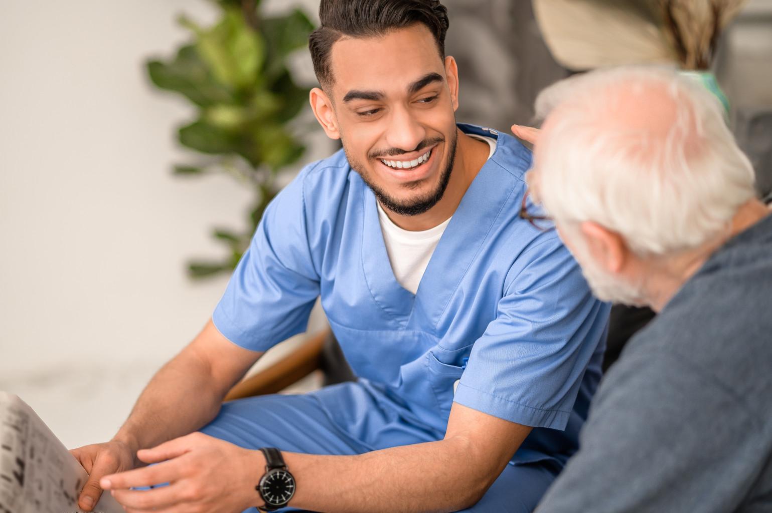 Pfleger mit Migrationsgeschichte unterhält sich mit älterem Mann 