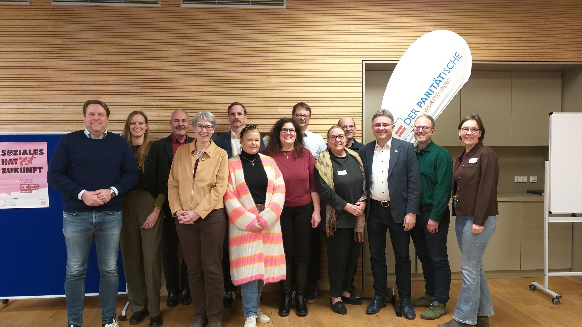 Vor dem Logo des Paritätischen posieren die Teilnehmenden der Veranstaltung: Paritätischer Kreisvorstand Mannheim, Vertreter*innen der Mitgliedsorganisationen und die Kandidierenden