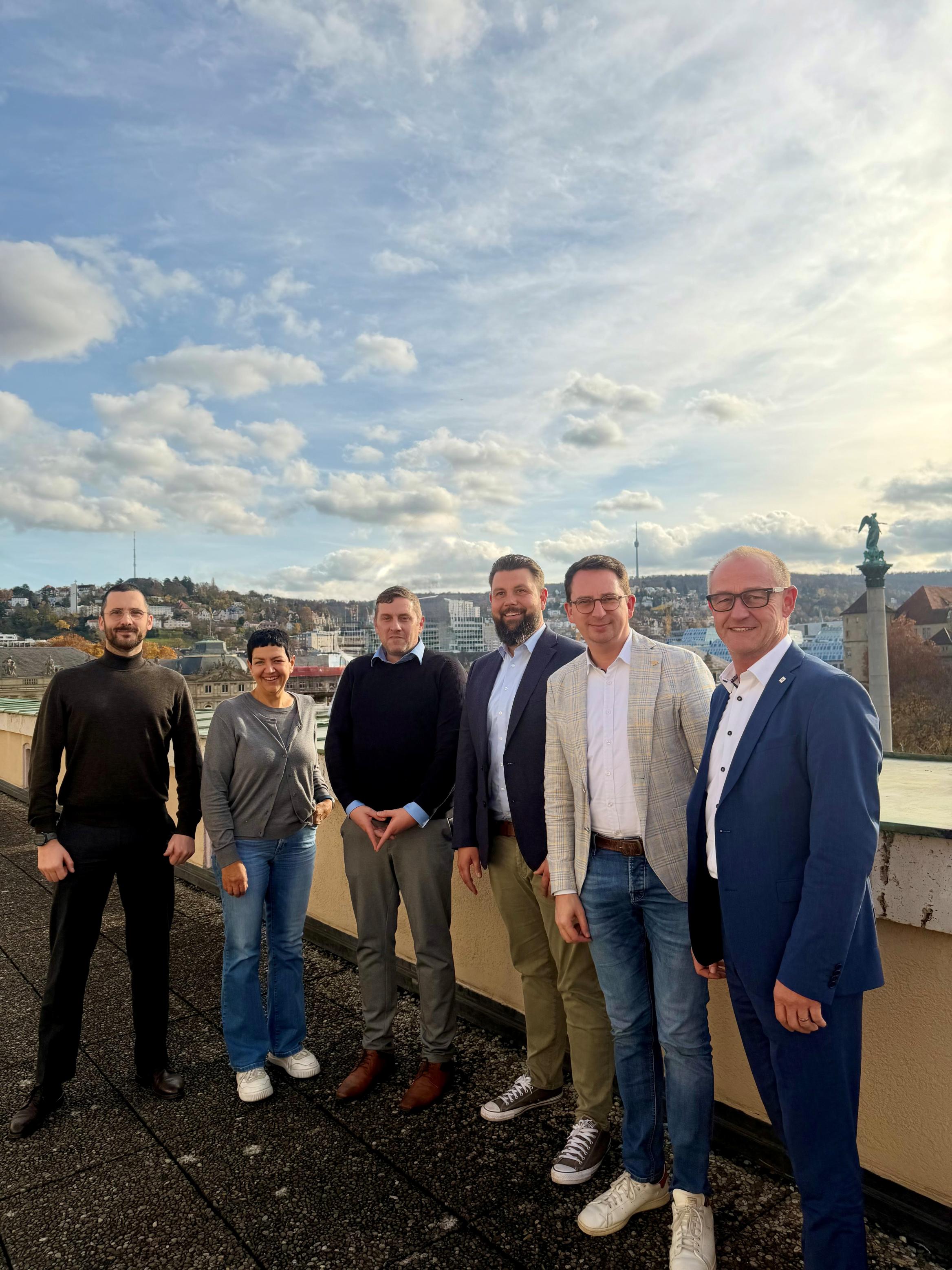 6 Personen stehen auf einer Dachterrasse mit Blick über Stuttgart und blauem Himmel