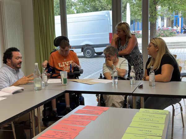 Workshopteilnehmende sitzen mit Referenten am Tisch