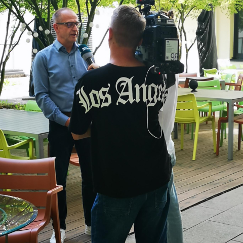 Kameramann und Reporterin mit Ulf Hartmann im Innenhof mit Vorstand vor Bäumen