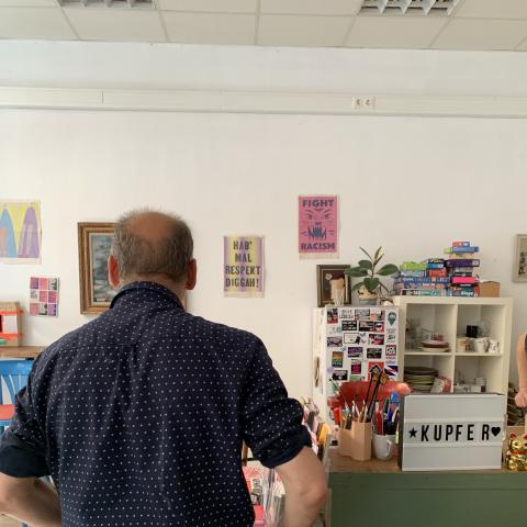 ein Mann in dunklem Hemd von hinten in einem helle Raum