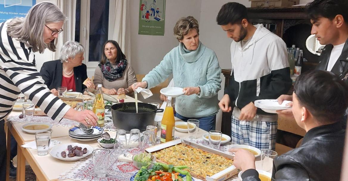 Menschen an einem gedeckten Tisch, an dem das Essen verteilt wird