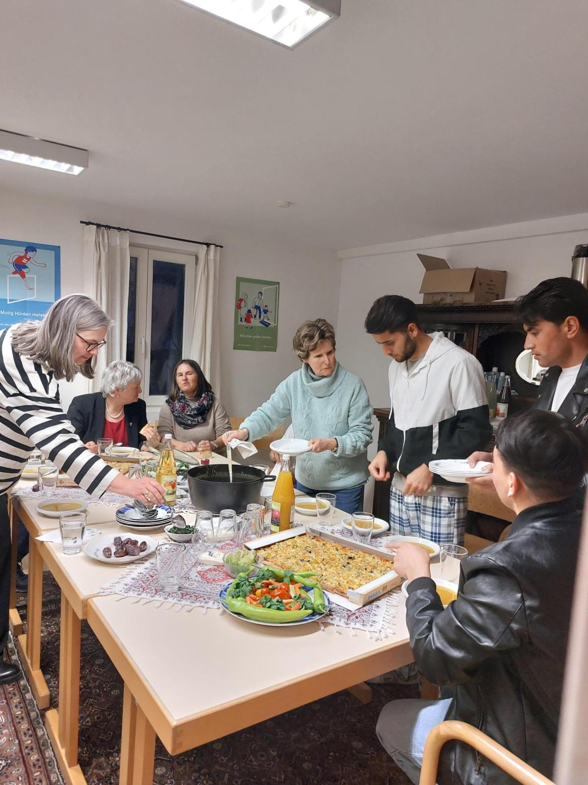 Menschen an einem gedeckten Tisch, an dem das Essen verteilt wird
