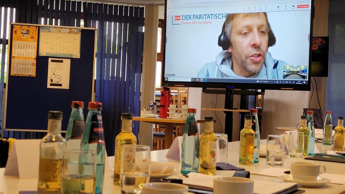 Tagungssituation; Getränke auf dem Tisch und großer Bildschirm mit Michael Tränkle drauf