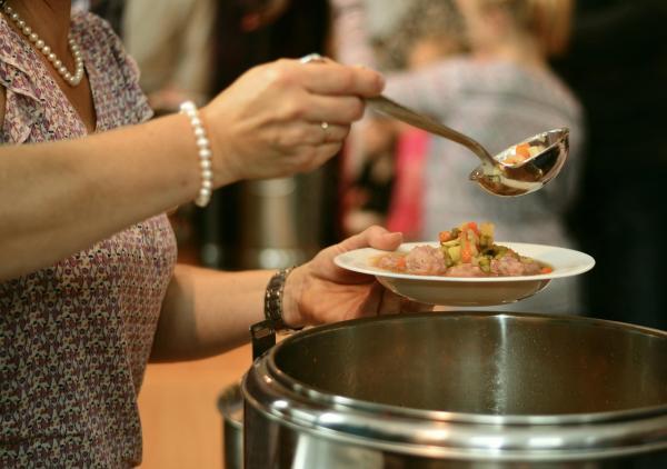 Frau holt sich Essen mit Suppenkelle aus Kochtopf