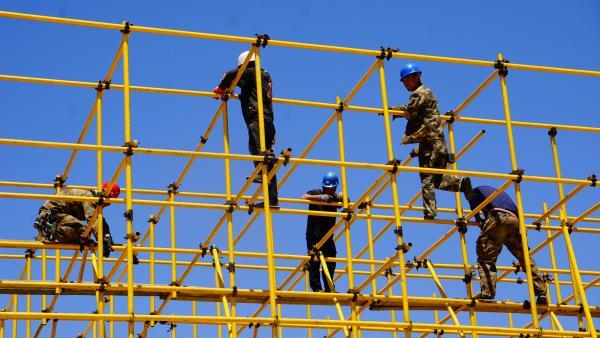 Handwerker auf einem gelben Gerüst vor blauem Himmel