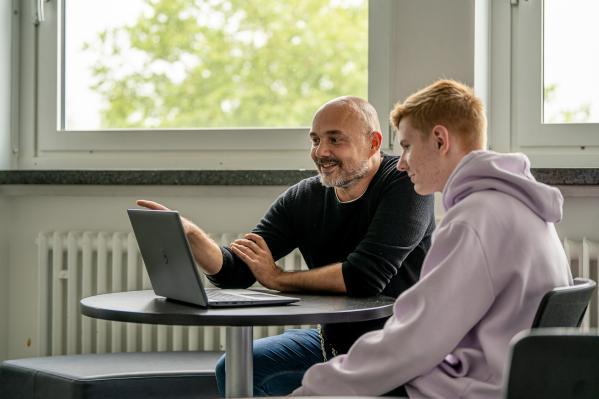ein junger Mann schaut einem Berater an einem Tisch in einen Laptop