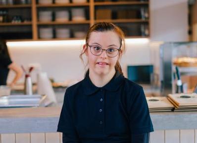 Junge Frau mit Downsyndrom sitzt vor einer Restaurantbar