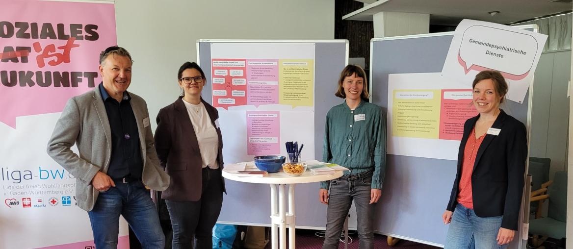 Informieren über Gemeindepsychiatrie und stehen vor den Stellwänden und dem Roll-up der Liga mit der Aufschrift "Soziales ist (durchgestrichen) hat Zukunft": Jürgen Maurer, Gianna Wetzel, Ida Wehinger, Annika Beutel
