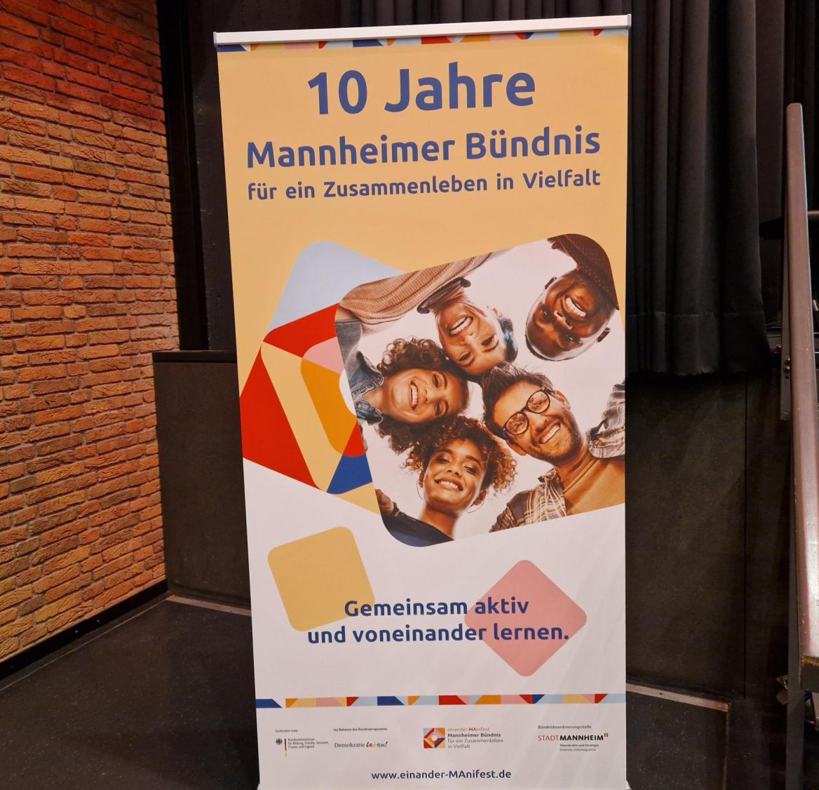 &Uuml;berschrift des Plakats: 10 Jahre Mannheimer B&uuml;ndnis; 5 Personen stecken die K&ouml;pfe zusammen und l&auml;cheln in die Kamera.