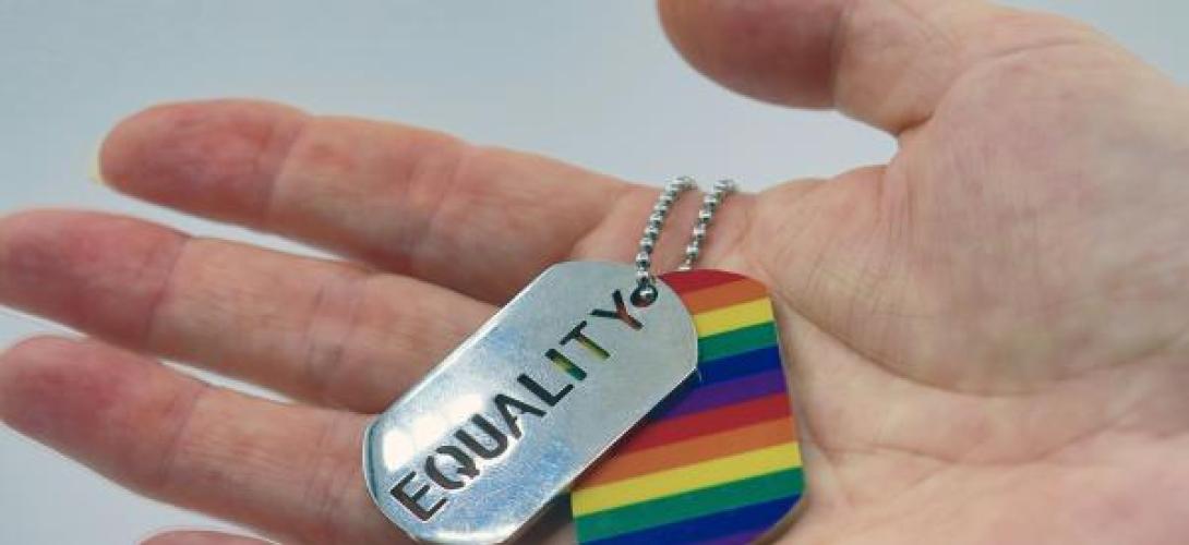 eine Hand hält einen Regenbofgen anhänger und eine Plakette mit Equality