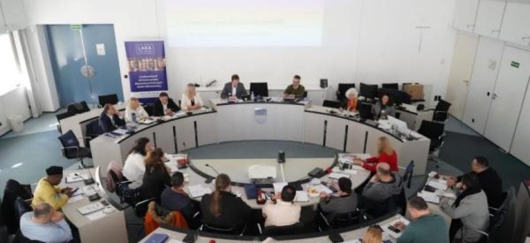 große Beratungsrunde mit vielen Menschen an im Kreis platzierten Tischen