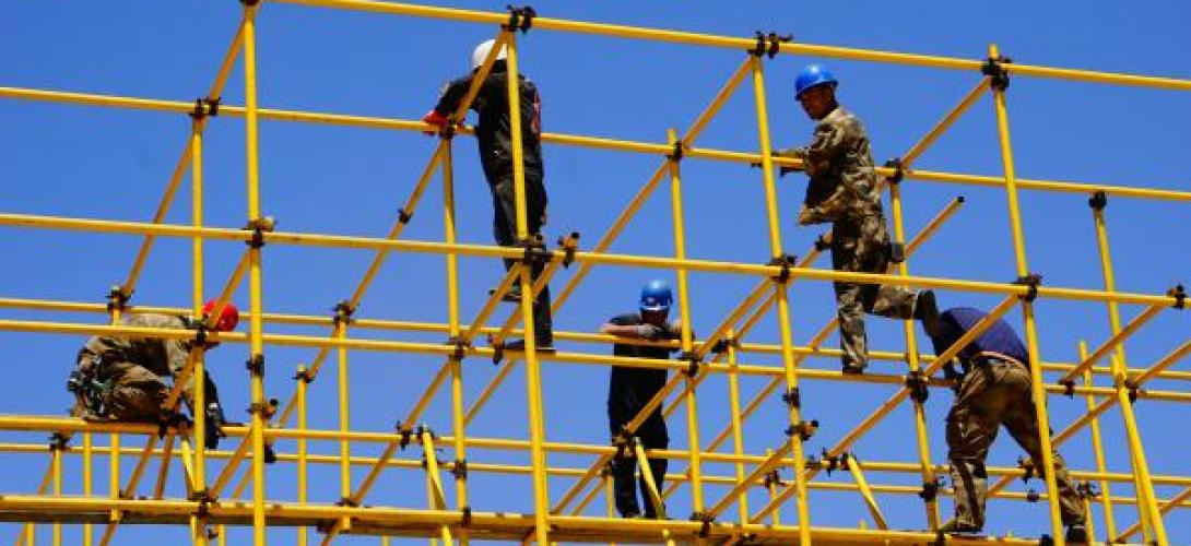 Handwerker auf einem gelben Gerüst vor blauem Himmel