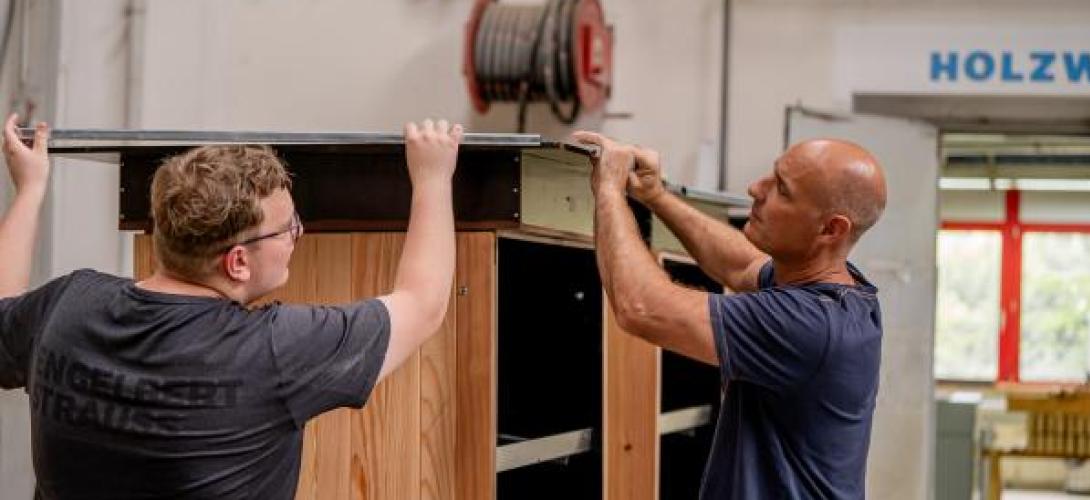 zwei Männer arbeiten an einem Holzschrank in einer Werkstatt