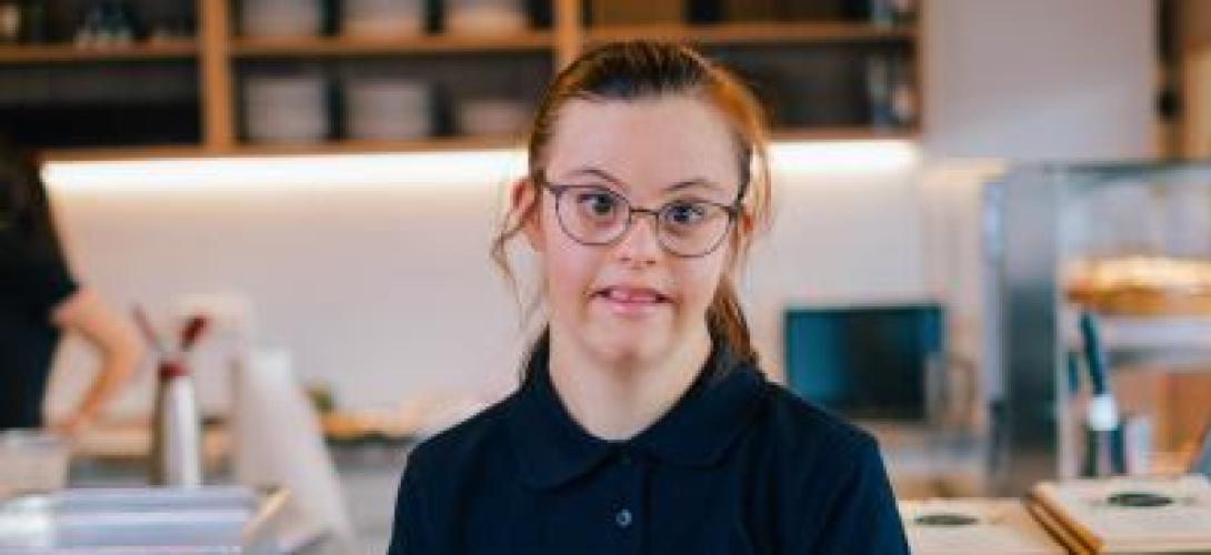 Junge Frau mit Downsyndrom sitzt vor einer Restaurantbar