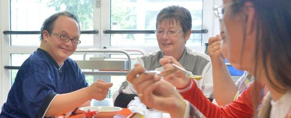 Menschenmit Behinderung und Betreuerinnen sitzen gemeinsam beim Essen am Tisch