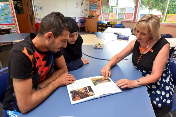 Frau sitzt mit einem mann und Kind an einem Tisch und deutet auf ein Bild in einem Buch