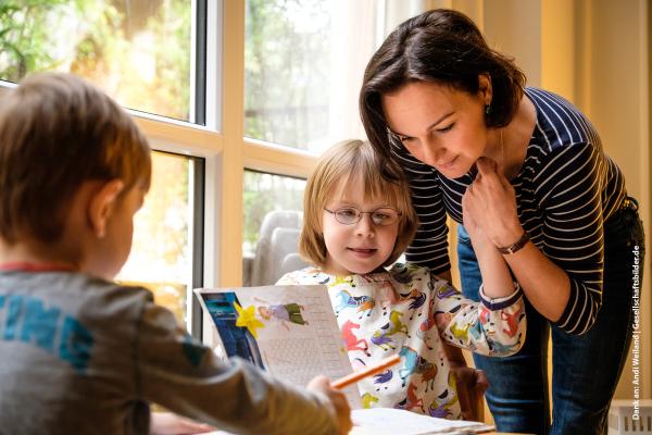 Zwei Kinder zuhause am Tische malend mit Frau