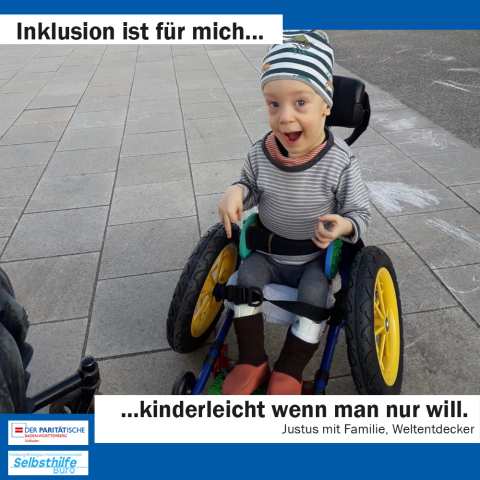 Ein kleiner Junge sitzt stolz und frech in seinem Miniatur-Lego-Rollstuhl mit Kinderwagenrädern als Greifreifen. Darunter steht: "Inklusion ist für mich kinderleicht wenn man nur will. Justus mit Familie, Weltentdecker"
