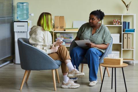 Afrikanische Sozialarbeiterin spricht mit einem schwierigen Mädchen im Teenageralter, während sie im Büro auf Sesseln sitzen