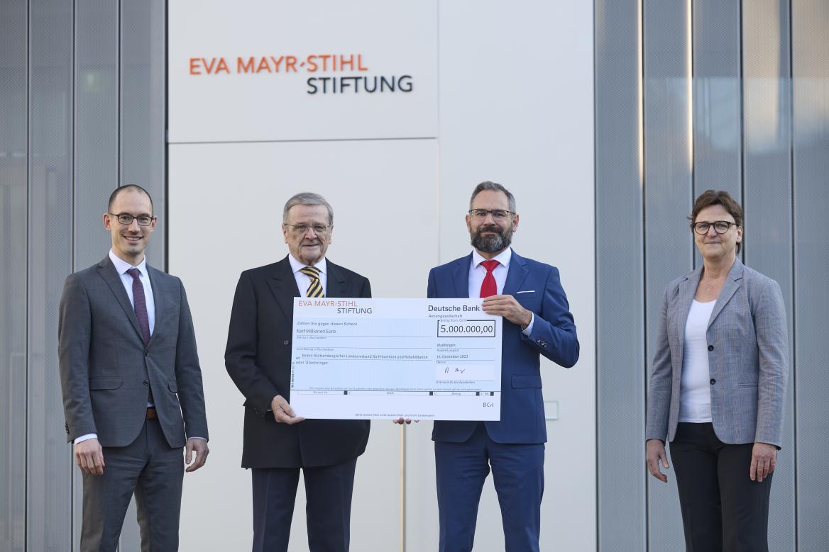 Drei M&auml;nner und eine Frau stehen nebeneinander mit Scheck in der Hand