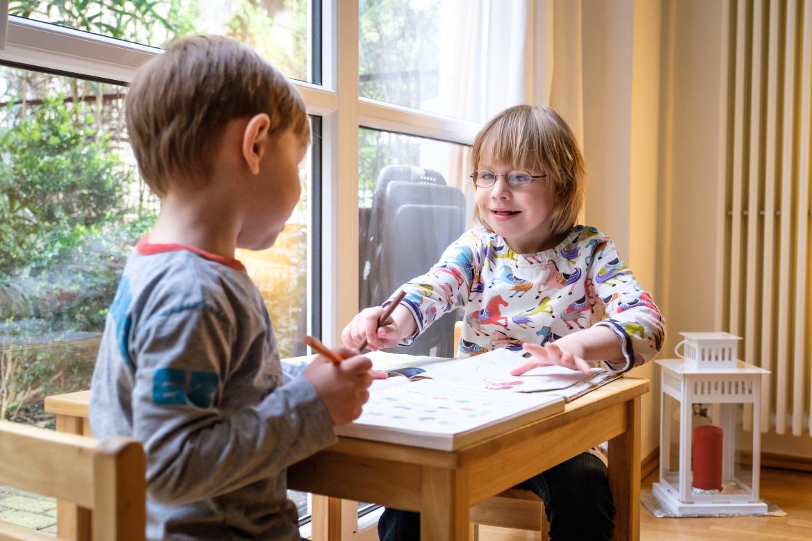 Kleiner Junge und kleines M&auml;dchen mit Behinderung sitzen gemeinsam am Tisch und Malen
