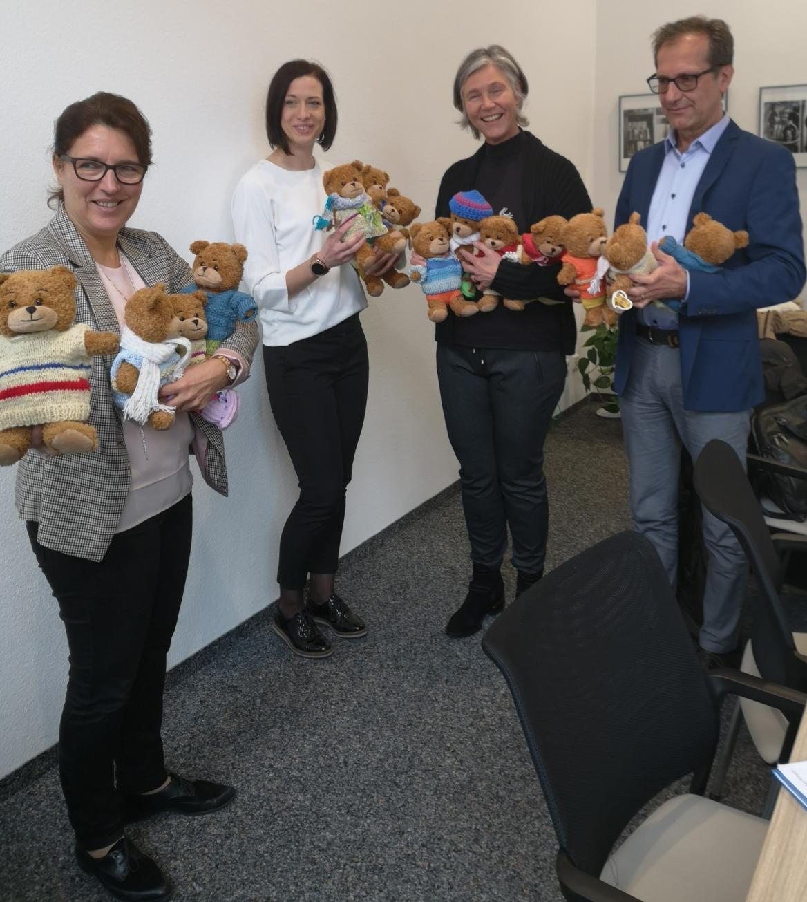 drei Frauen  und ein Mann stehen im Halkreis und halten Teddyb&auml;ren in Strickkleidung in den H&auml;nden