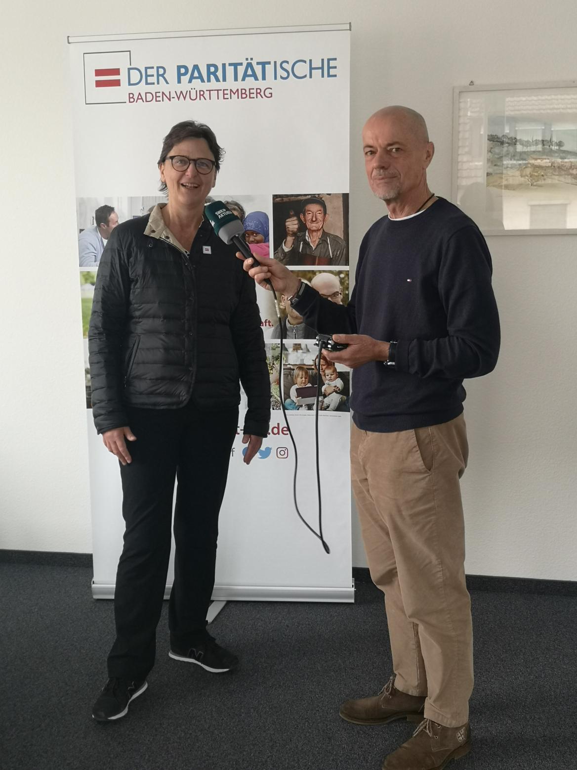 Mann interviewt Frau vor Banner stehend