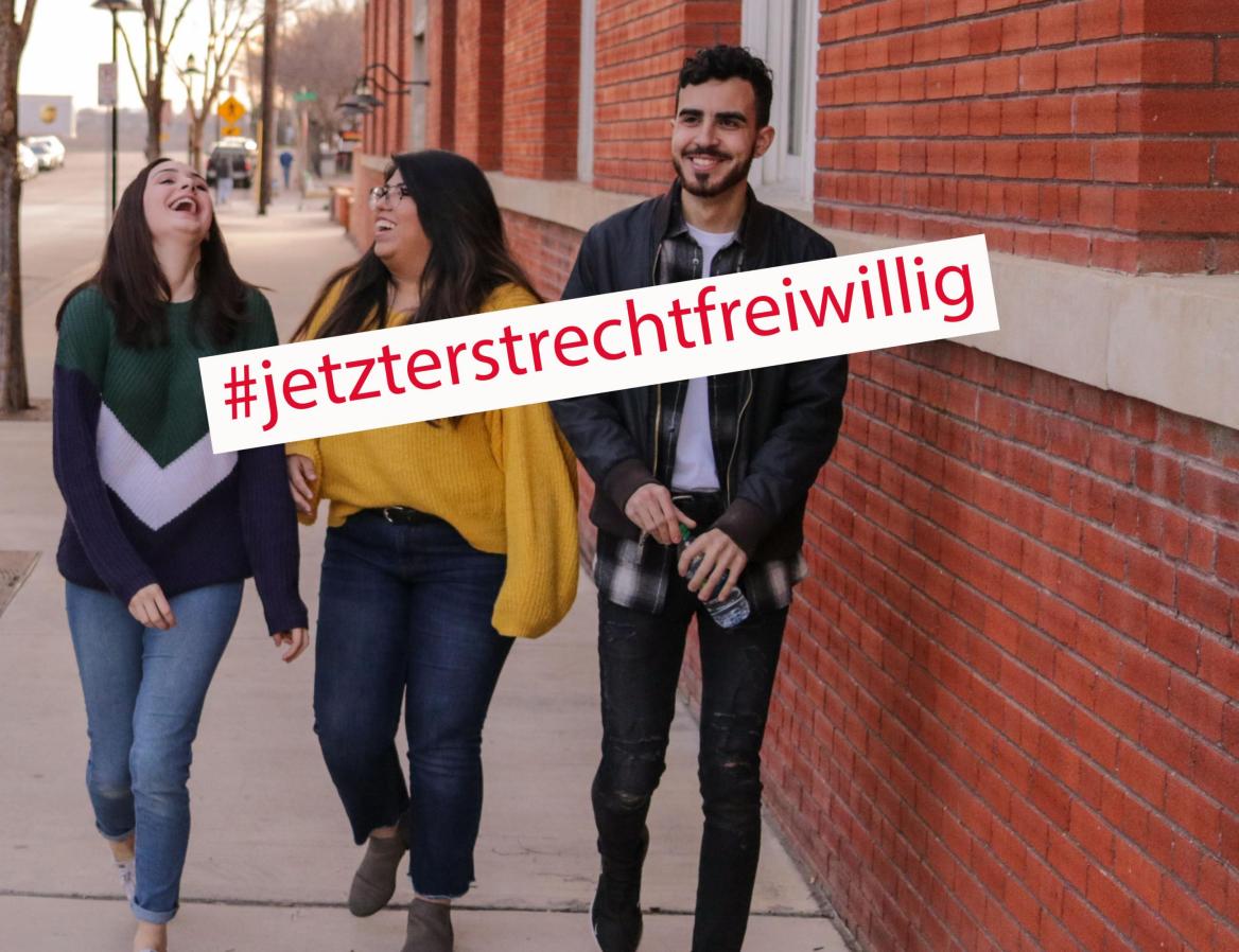 Drei Menschen gehen nebeneinander her und lachen. Auf dem Bild steht der Slogan "#jetzterstrechtfreiwillig"