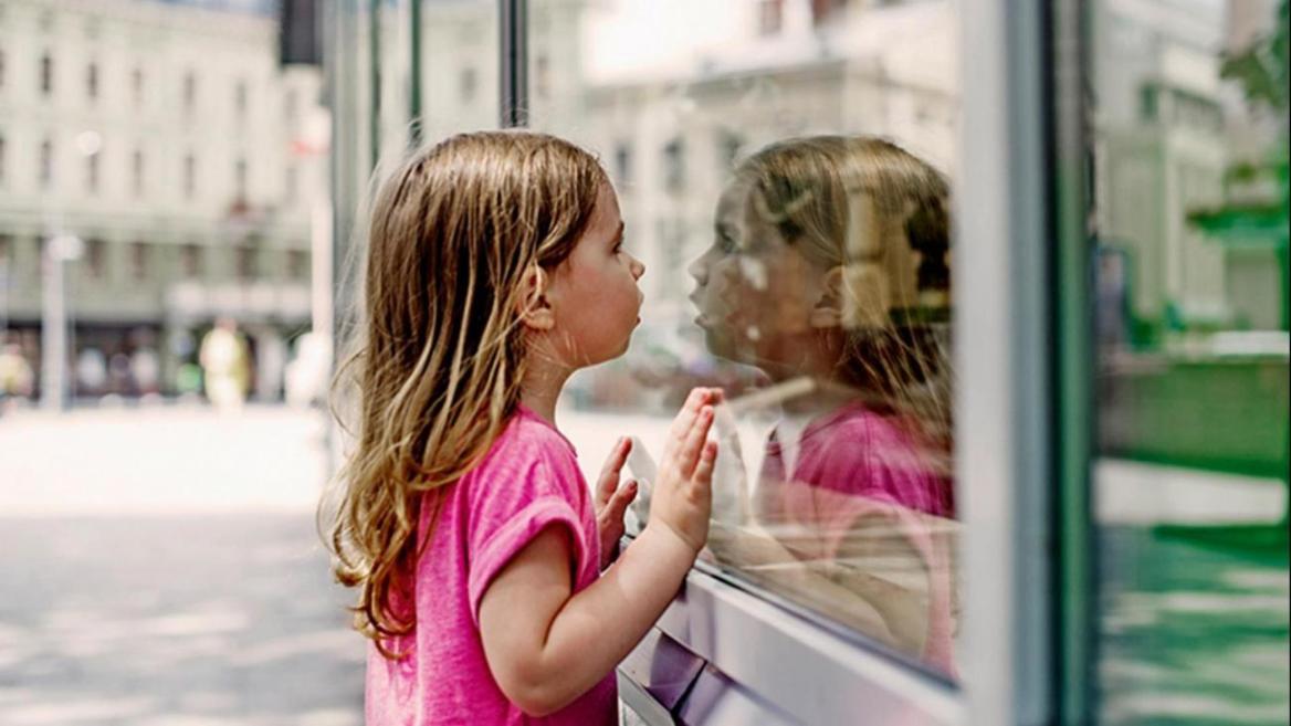 Ein junges M&auml;dchen schaut ins Fenster und spiegelt sich