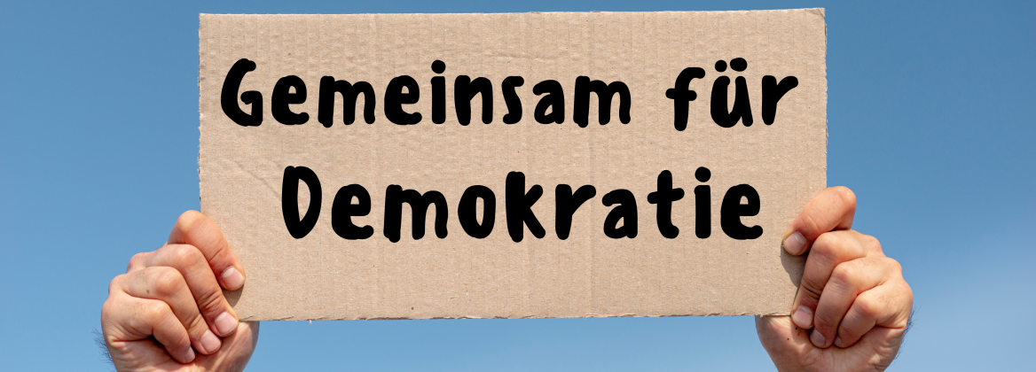 Schild mit gemeinsam f&uuml;r Demokratie wird mit zwei H&auml;nden hochgehalten