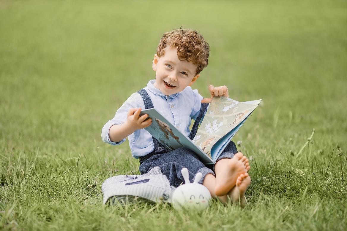 Kind sitzt mit Buch auf Rasen