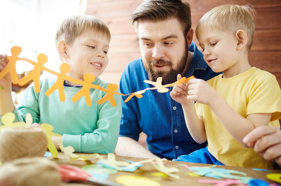junger Mann bastelt mit 2 Kindern mit Papier
