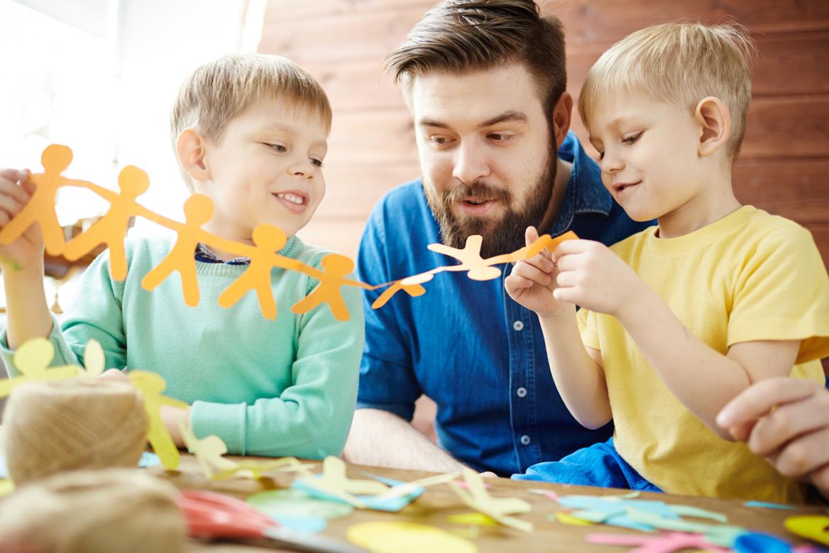 junger Mann bastelt mit 2 Kindern mit Papier